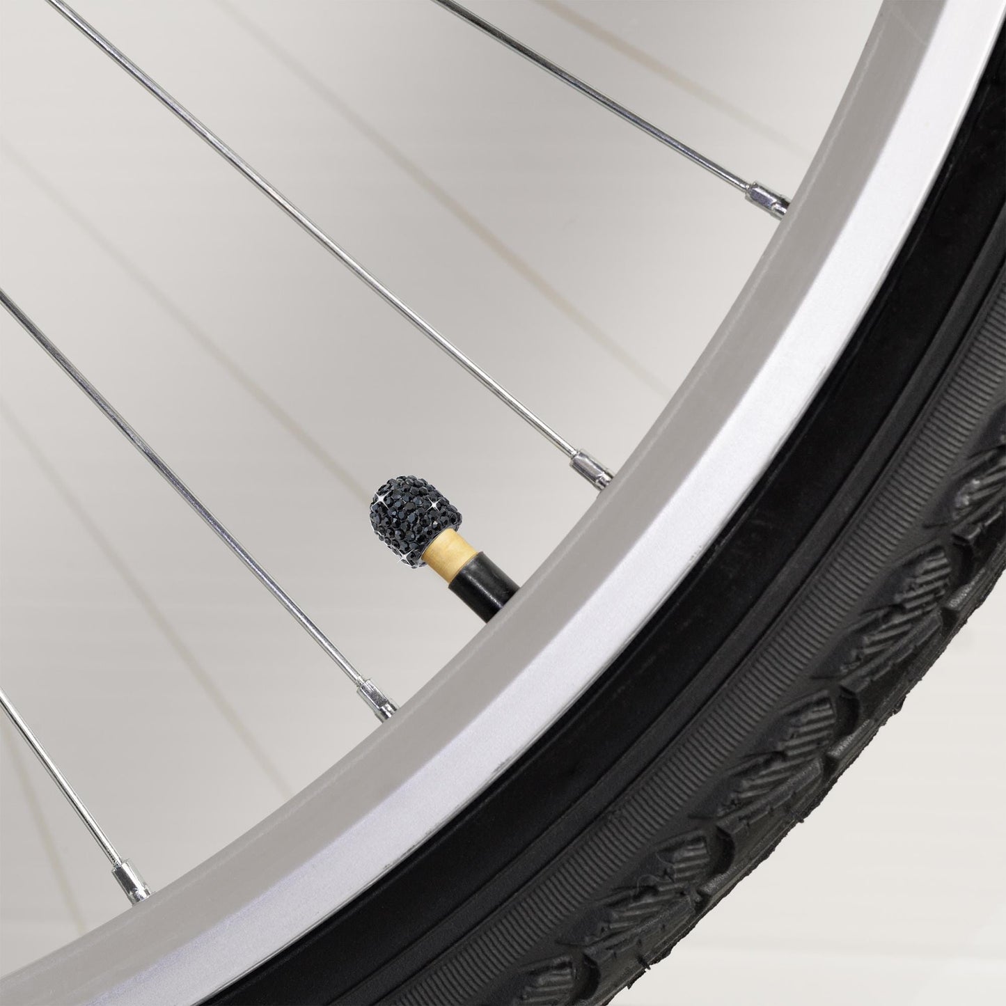 Black rhinestone tire valve caps on bicycle wheel close-up
