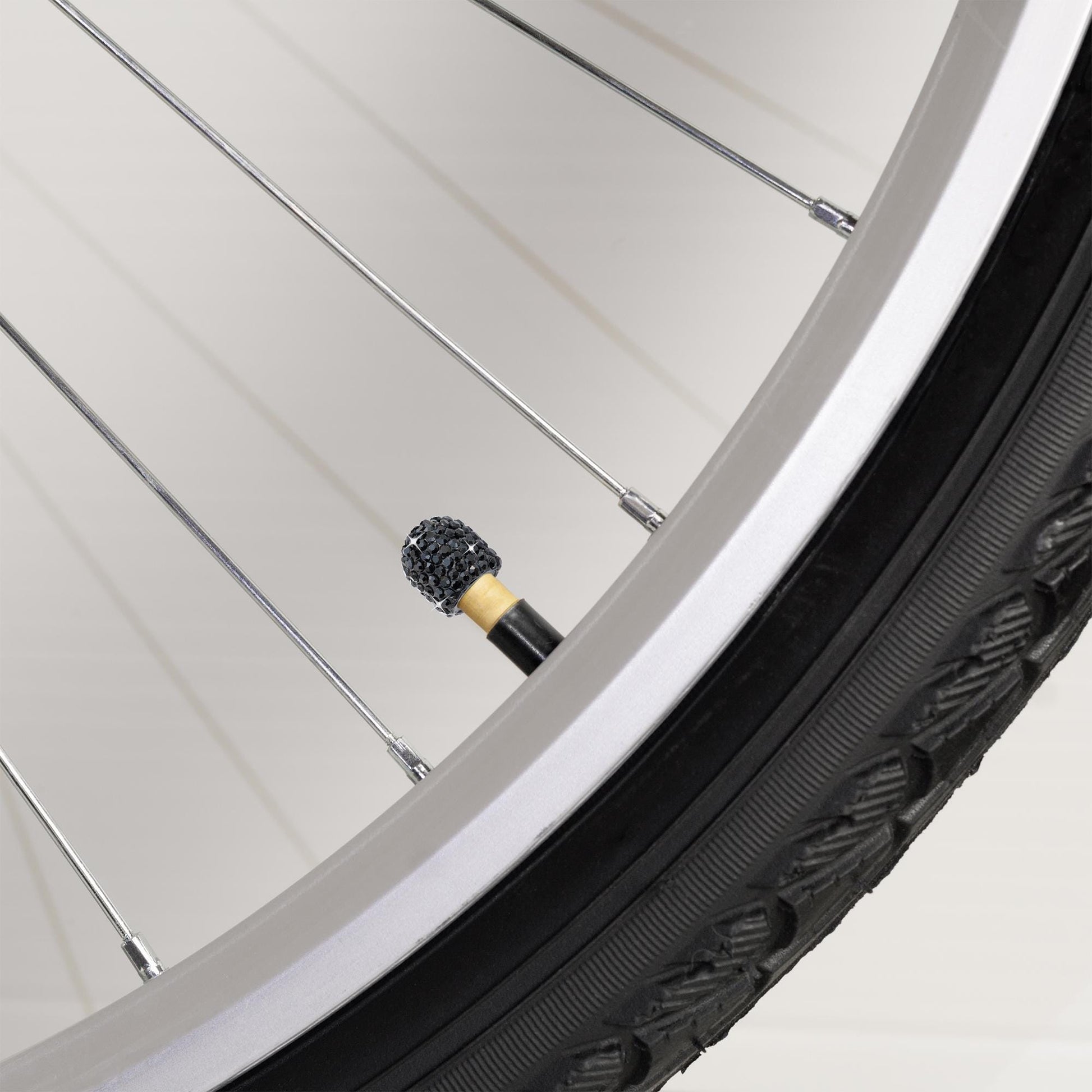 Black rhinestone tire valve caps on bicycle wheel close-up
